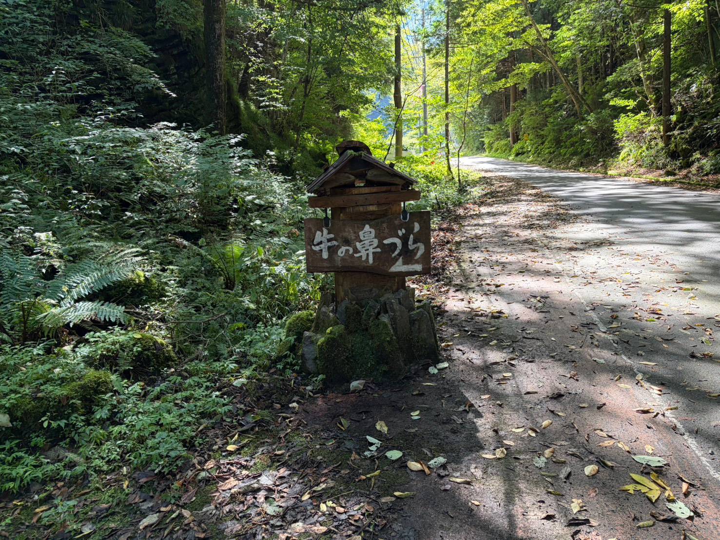 道端に立つ牛の鼻づらの木の立て札。小屋根と石積みの土台がついている