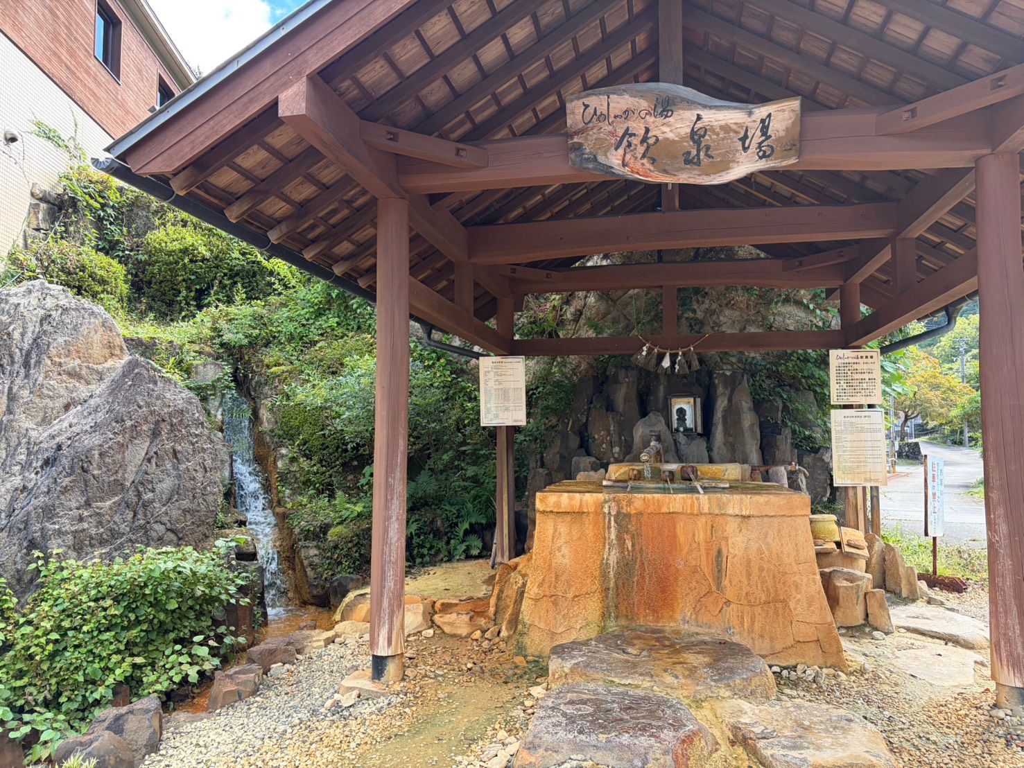ひめしゃがの湯の飲泉場。ヒノキの東屋の下に、湯で染まった岩の湯船がある